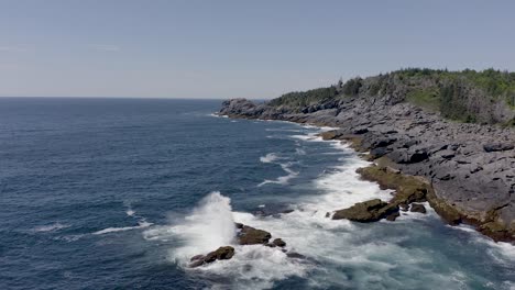 drone flyine low along the water as a big wave crashes on the rocky coastline in maine