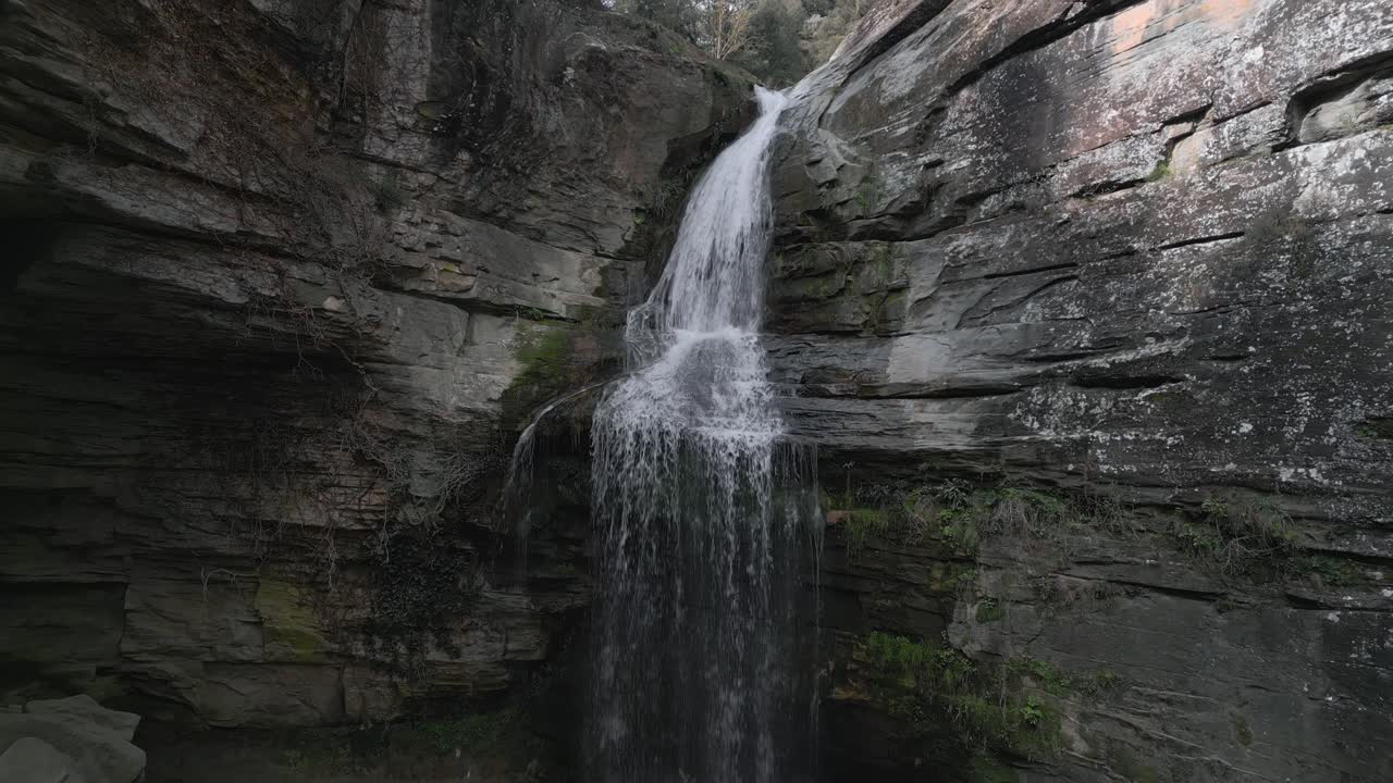 Crystal clear water gracefully flows over a rocky cliff face, creating a picturesque waterfall in the natural landscape of catalonia, near barcelona