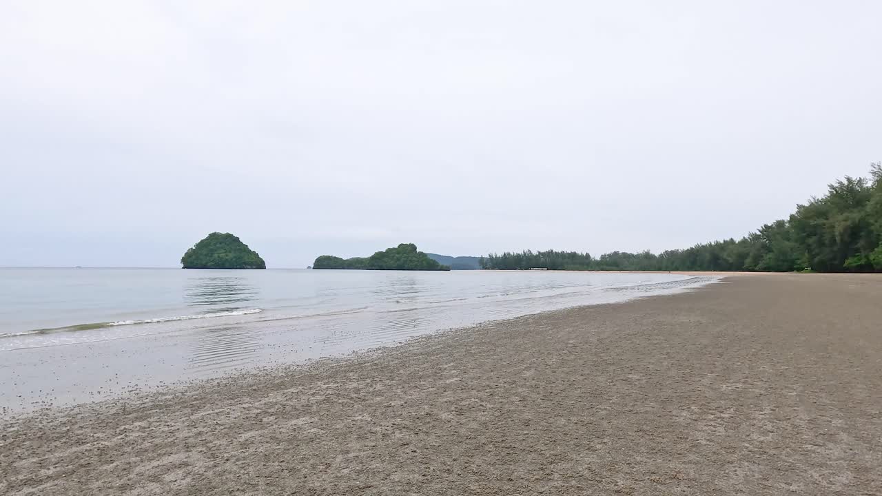 A tranquil beach in Krabi, Thailand, showcasing calm waters and lush greenery under soft, overcast lighting