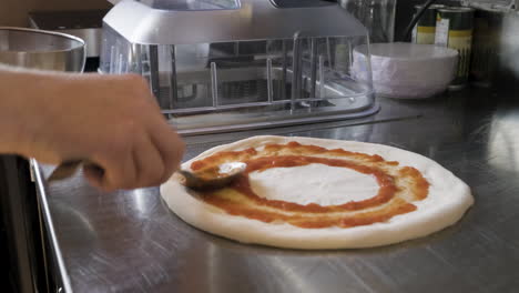 close up view of a chef hands spreading sauce on pizza dough on a restaurant kitchen countertop