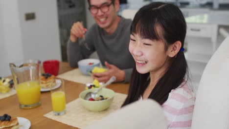 happy asian father in kitchen eating breakfast with laughing son and daughter