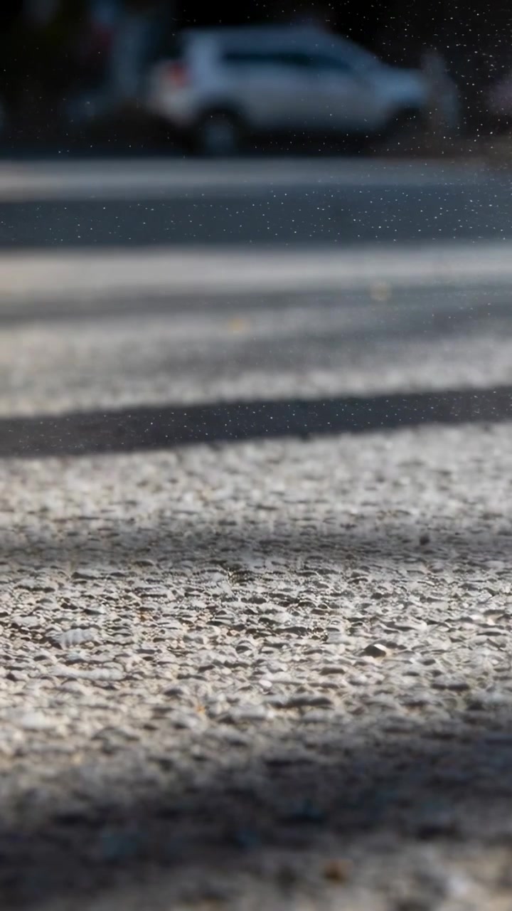 Video verticale: Brezza che solleva pulviscolo, attraversando ombre illuminate dal sole sul marciapiede, vicino al cordolo, con un'auto parcheggiata.