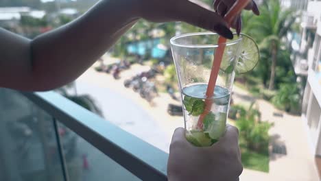 la dama en el balcón agita un cóctel de mojito en un vaso medio vacío