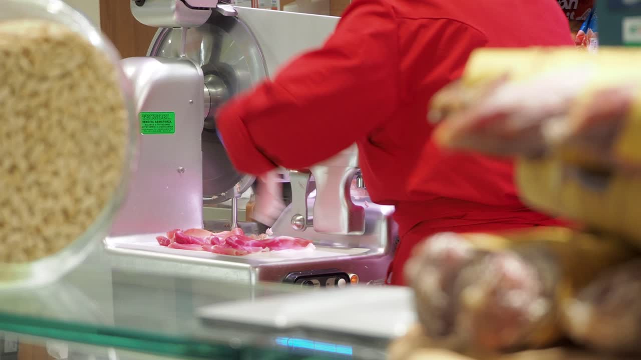 Butcher using a meat slicer to cut meat in a deli