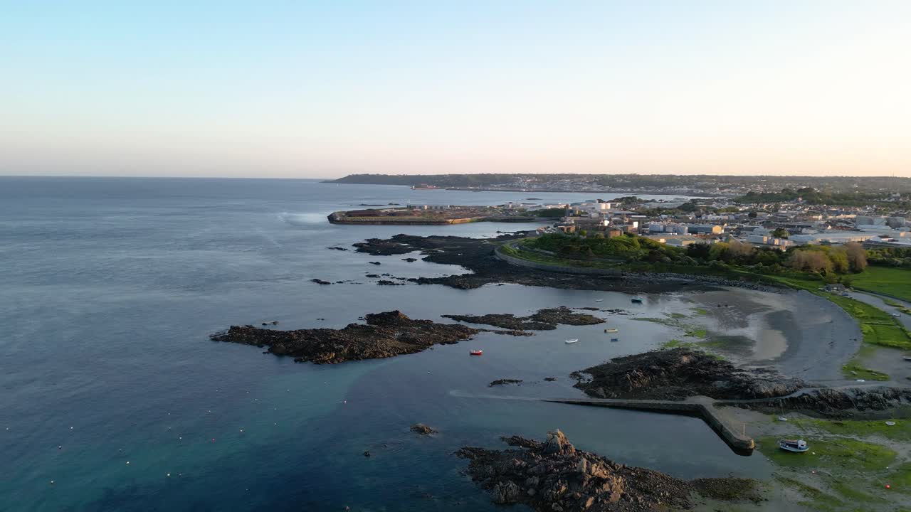 Volo sopra il Porto di Bordeaux e una spiaggia di Guernsey, guardando verso St Sampsons e St Peter Port in lontananza, a metà marea in un tardo pomeriggio luminoso con cielo sereno e mare calmo
