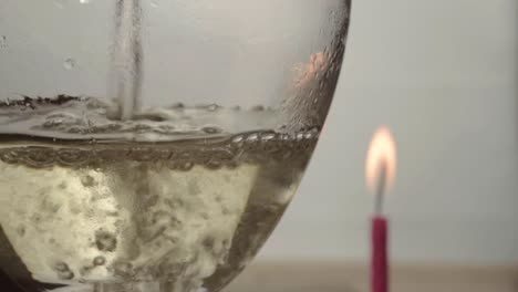 pouring glass of white wine with candle in background close up shot