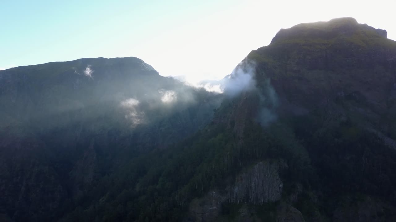 volando hacia las cimas de las montañas de madeira, portugal con nubes besando la ladera de la montaña - toma aérea