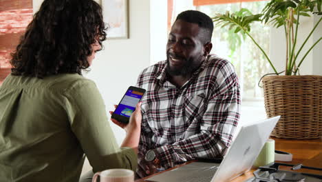 multiracial couple discussing plans using smartphone and laptop at home