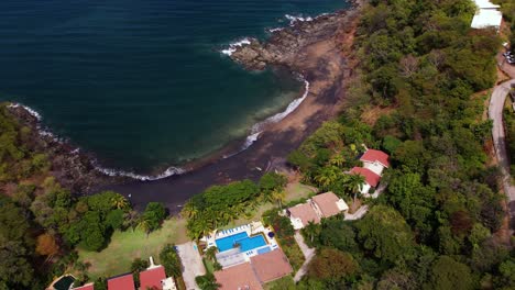 aerial of various semi-detached chalets at foot of a tropical volcanic sand beach of costa rica