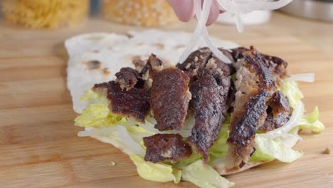 slow motion slider shot of adding finely sliced onions to a doner kebab in naan bread at home in the kitchen