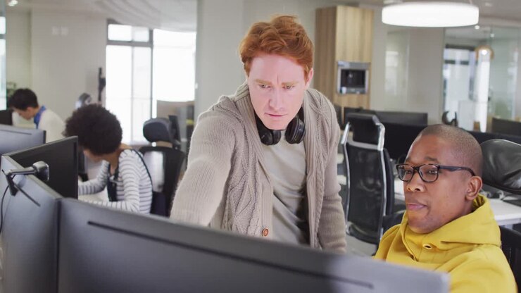 Diverse male business colleagues pointing at computer and discussing in office