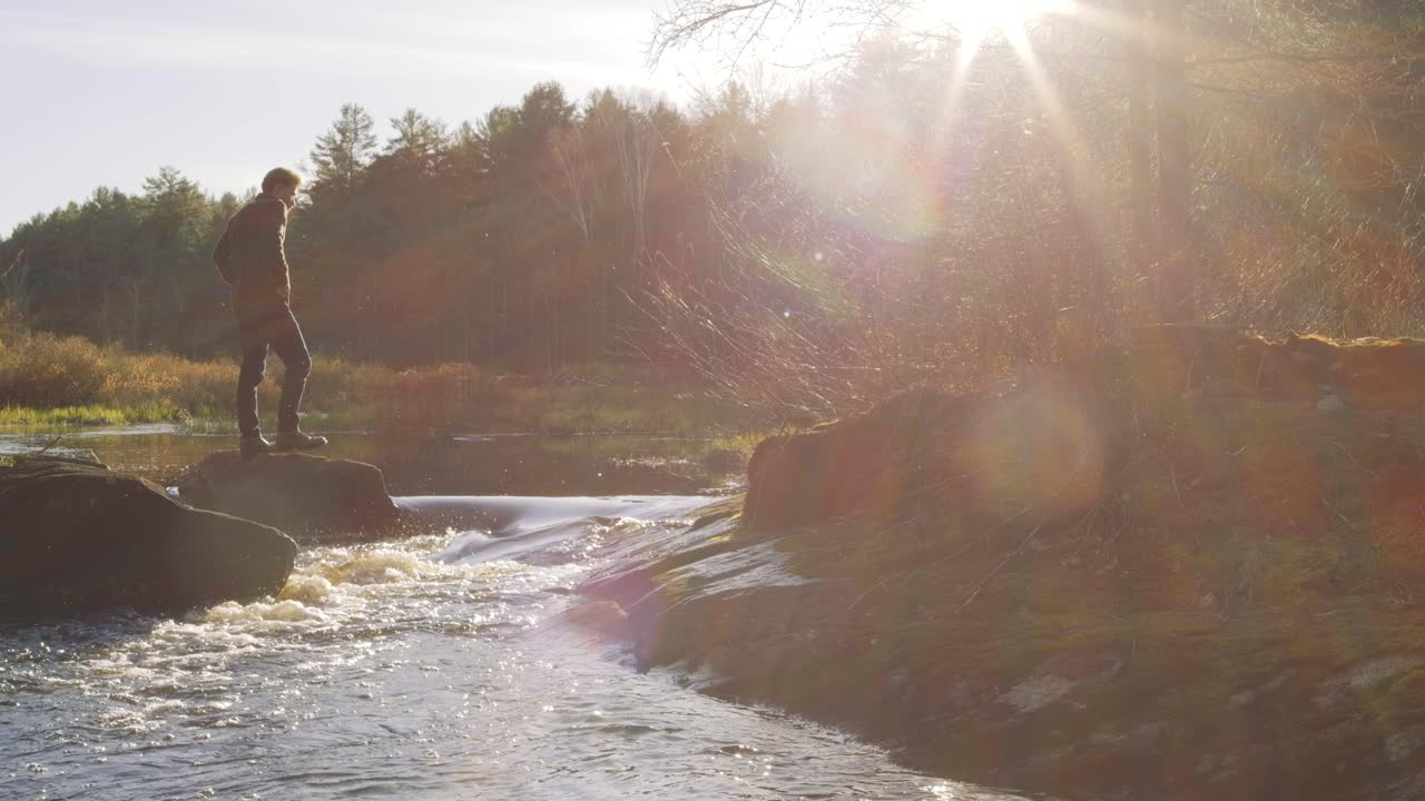 hombre de pie en una roca junto a un río en un bosque al amanecer, rodeado de naturaleza y bañado en la luz de la mañana