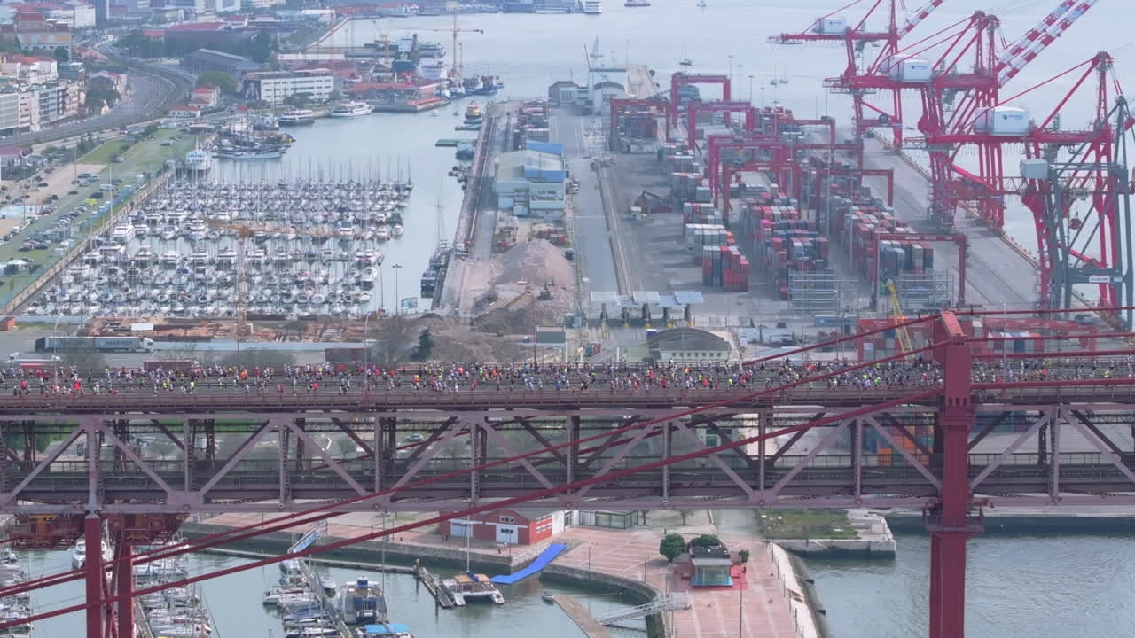 Side-on aerial drone shot of half marathon and 10K long-distance running event in Lisbon, Portugal, Europe. Runners crossing the iconic red 25th April bridge