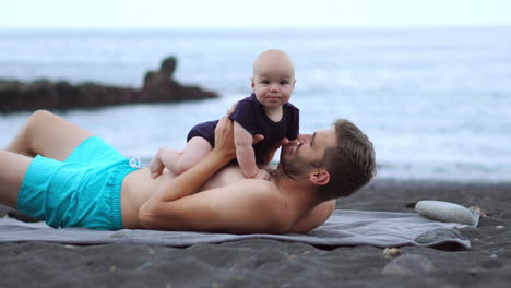 By-the-beach,-a-young-dad-enjoys-playful-exchanges-with-his-newborn-son.-These-valuable-instances-enhance-his-vacation,-showcasing-his-elation-as-a-contented-father