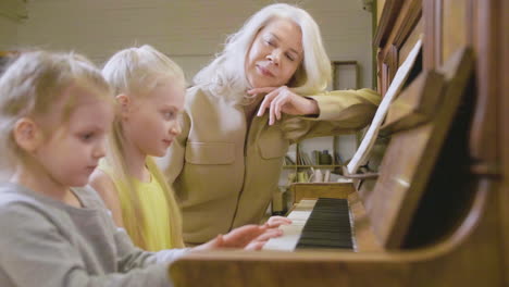 dos niñas pequeñas tocando el piano viejo en casa mientras su abuela las observa