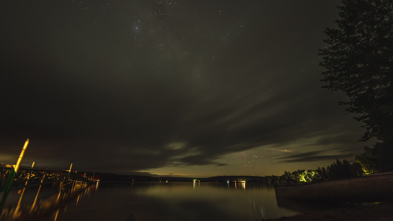 Un timelapse notturno dalla spiaggia di un cottage in riva al lago mentre nuvole, stelle e la Via Lattea passano.
