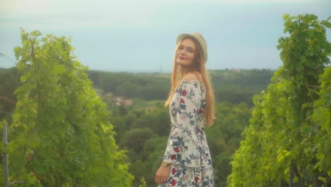 Stunning-HD-footage-of-a-Caucasian-girl-with-a-knitted-hat-and-red-lipstick-standing-in-a-vineyard,-illuminated-by-sunlight,-looking-and-smiling-into-teh-camera