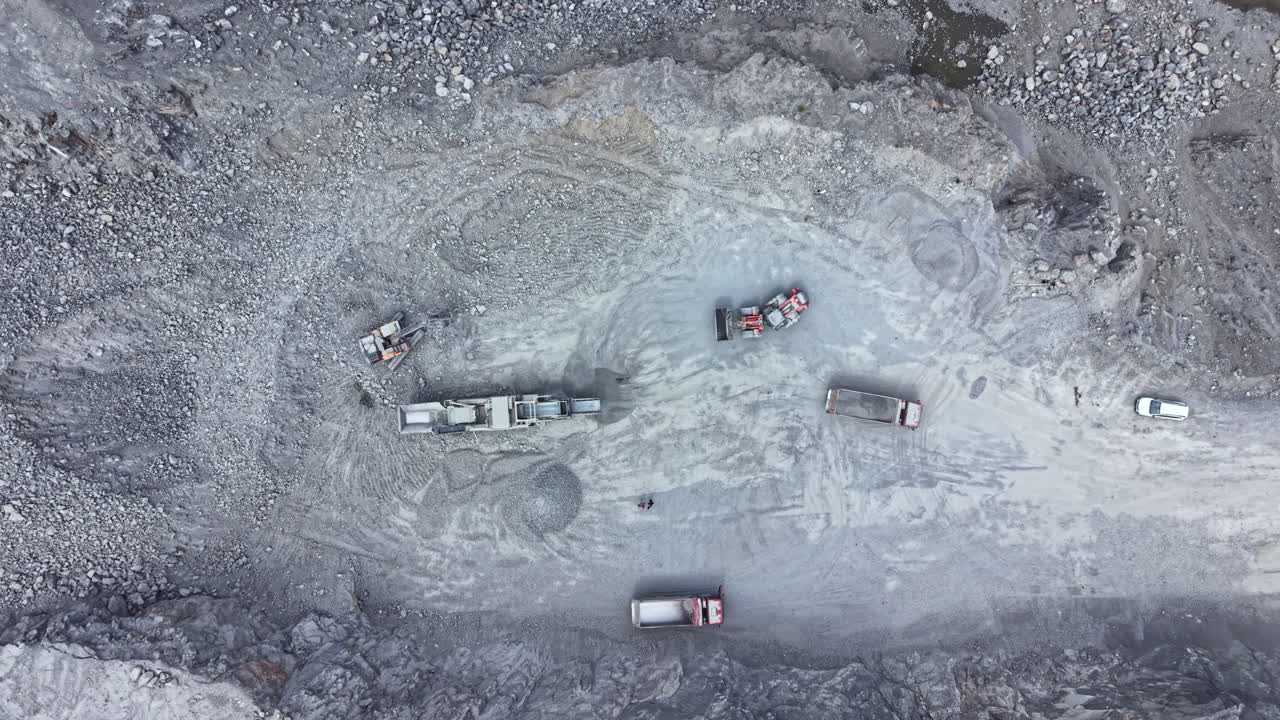 Heavy machinery works on a construction site with trucks and equipment moving materials in a rocky landscape