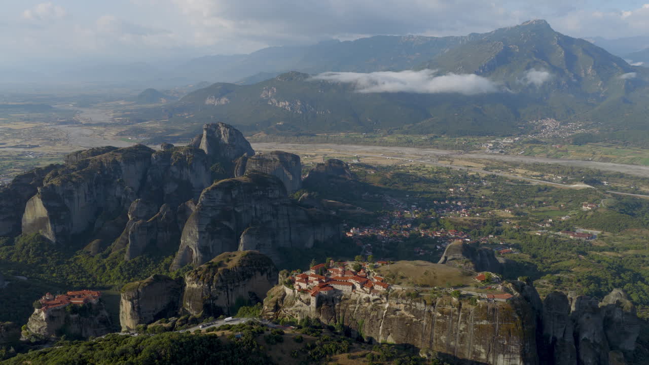 Cinematic aerial view of Meteora monastery in Greece perched on towering cliffs, dramatic rock formations and lush green valley create a breathtaking historic scene
