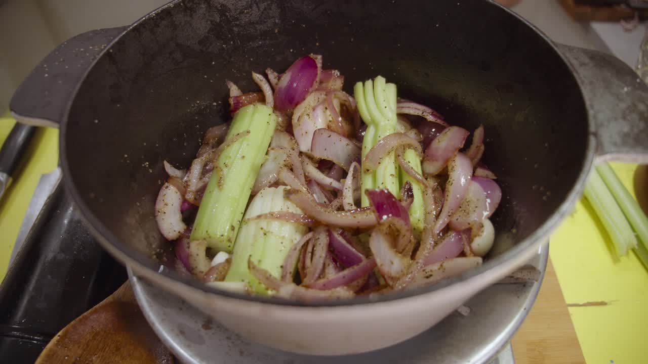 Stirring onion slices mixed with celery and spices with wooden kitchen spoon inside deep cooking pot