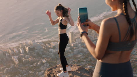 girl friends taking photo on mountain top using smartphone camera beautiful young woman posing for friend with mobile phone sharing hiking adventure on social media