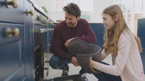 father with teenage daughter taking freshly baked homemade cupcakes out of the oven