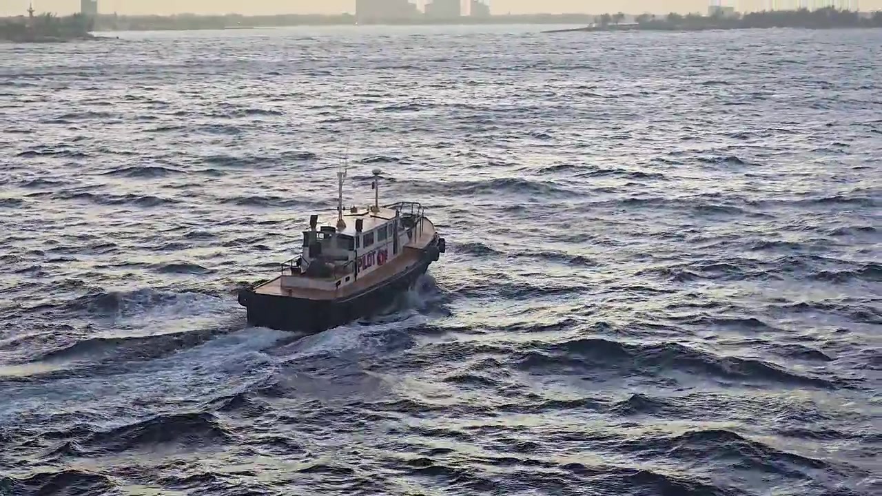 Una barca pilota naviga attraverso acque oceaniche agitate. La piccola imbarcazione marittima solca il mare, lasciando una scia bianca dietro di sé mentre si dirige ad assistere navi più grandi in acque aperte