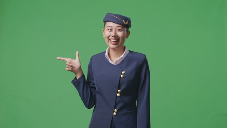 아시아 여성 승무원이 미소 짓고 녹색 스크린 배경 스튜디오에 서서 을 가리키고 있습니다.