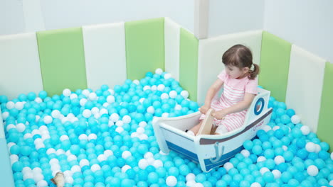 Glückliches-3-jähriges-Mädchen,-Kleinkind,-Das-In-Einem-Hölzernen-Spielzeugboot-Auf-Dem-Spielzeug-Trockenpool-Spielplatz-Schaukelt