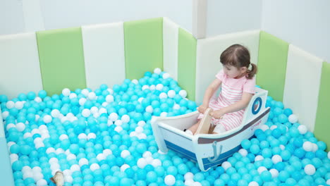 niña de 3 años de edad feliz niño pequeño balanceándose en un bote de juguete de madera dentro de un parque infantil de piscina seca de juguete
