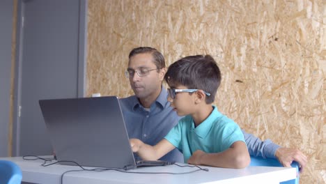 Teacher sitting near schoolboy in glasses