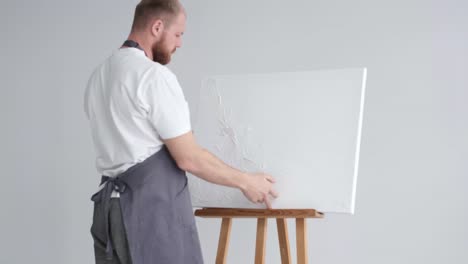 A Young Artist Sits at Home on a Stool in Front of a Canvas and Works with Inspiration Paints a