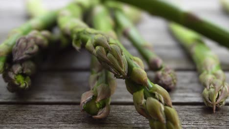 Aufnahmen-Von-Einem-Bund-Frischer,-Grüner-Spargel,-Der-Auf-Einen-Holztisch-Fällt