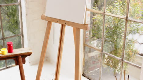 easel with colorful abstract painting near window in cozy art studio, at home