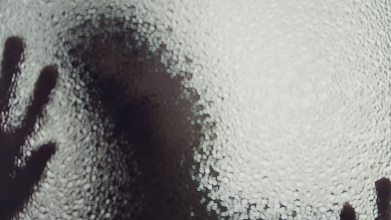 A female silhouette behind the frosted window touches the glass slowly