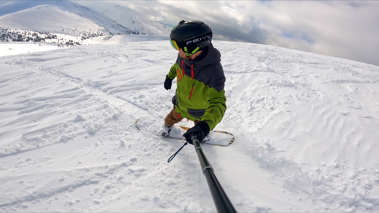 Sportsman taking selfie video of his snowboard ride down the hill. Active lifestyle in winter in the mountains.