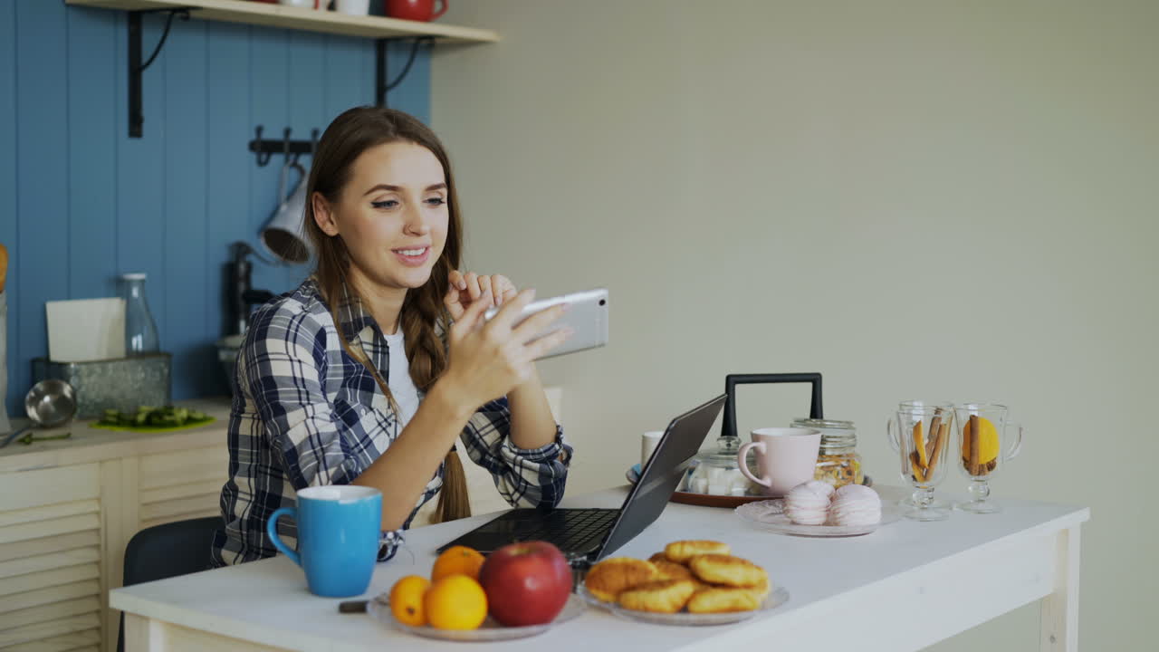 Woman using phone in kitchen, enjoying breakfast