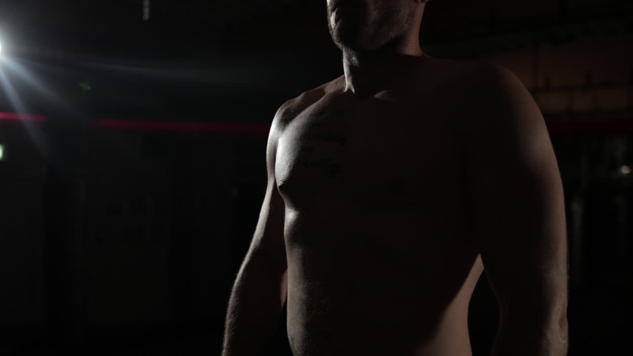 Primo piano medio, illuminato fiocamente, di un lottatore di MMA in piedi in una palestra