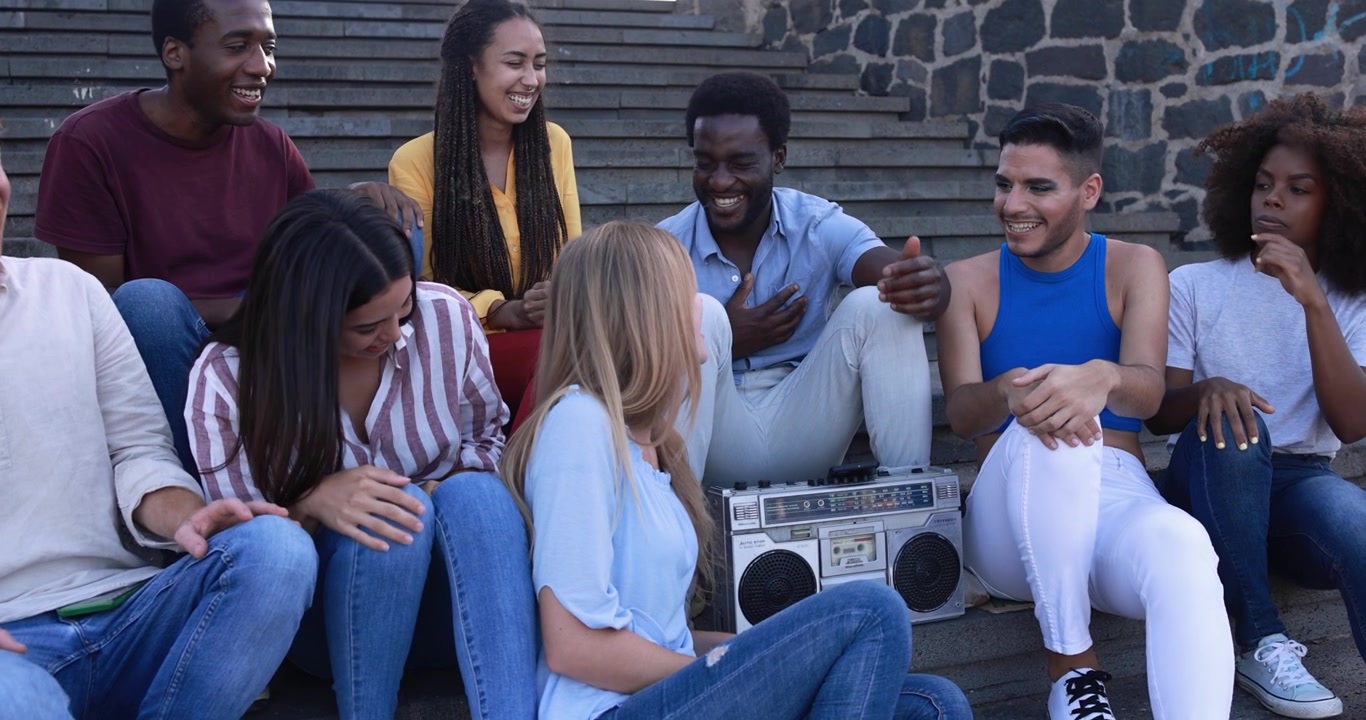 Vielfältige junge Freunde lachen und unterhalten sich auf einer Stadttreppe mit Boombox