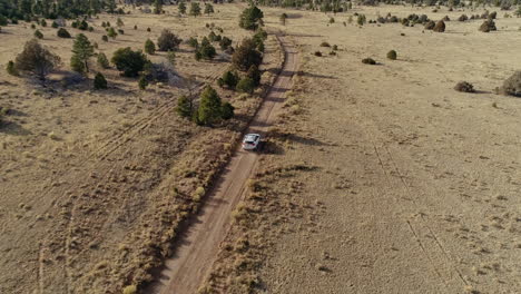 Tracking-aerial-on-white-car-traveling-down-remote-dirt-desert-road,-4K