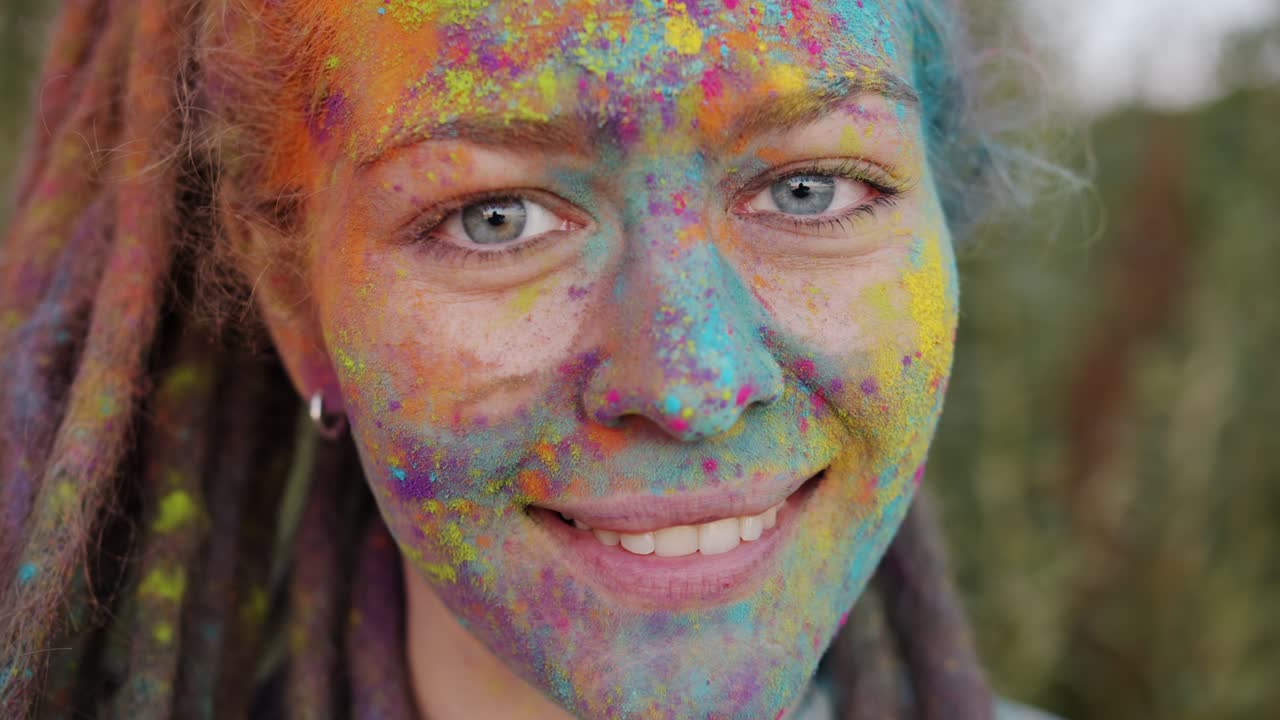 Close-up portrait of creative young woman with colorful face and dreads smiling outside
