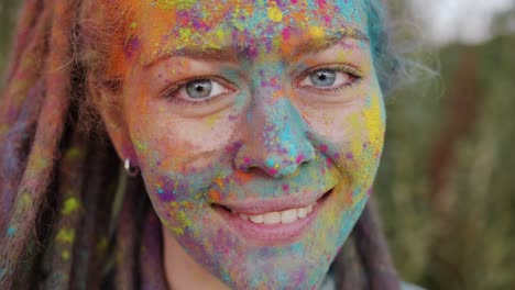 close-up portrait of creative young woman with colorful face and dreads smiling outside