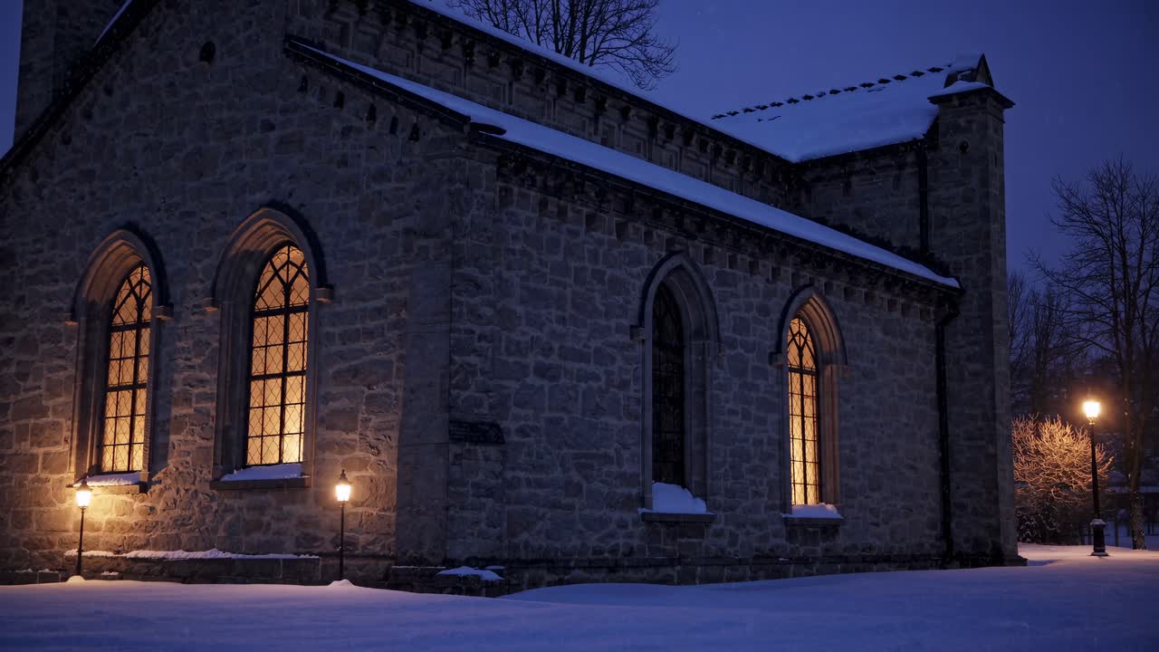 A serene video capturing a snow-covered church at dusk, with warm light glowing from windows, filmed