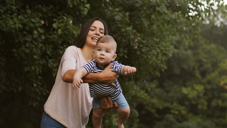 Glückliche-Junge-Mutter,-Die-Ihr-Süßes-Baby-Im-Arm-Hält-Und-Draußen-Als-Flugzeug-Schwingt-1