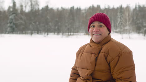 Vista-Frontal-Del-Hombre-Sonriente-Latino-En-El-Bosque-De-Invierno-Mirando-A-La-Cámara