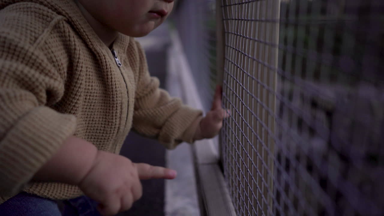 Cute baby boy pointing at landscape through protection grid. Hand held, close up