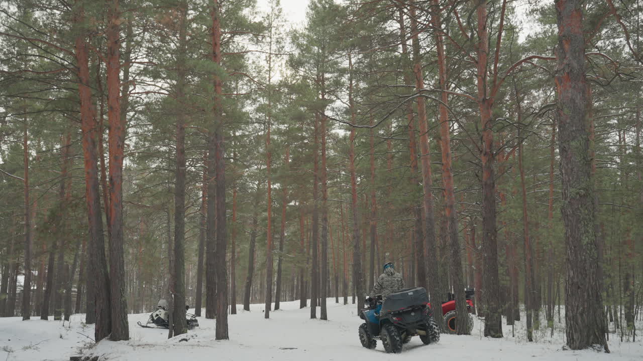 Un convoglio di ATV nella neve tra i pini si riunisce. Diversi piloti su quad colorati fanno una pausa sul sentiero innevato, veicoli rossi e blu si allineano. I piloti con casco controllano le mappe e chiacchierano, tracce di pneumatici sparse e neve.