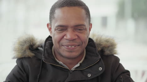 Afro-American-middle-aged-man-in-black-jacket-with-fur-hood-sitting-outside