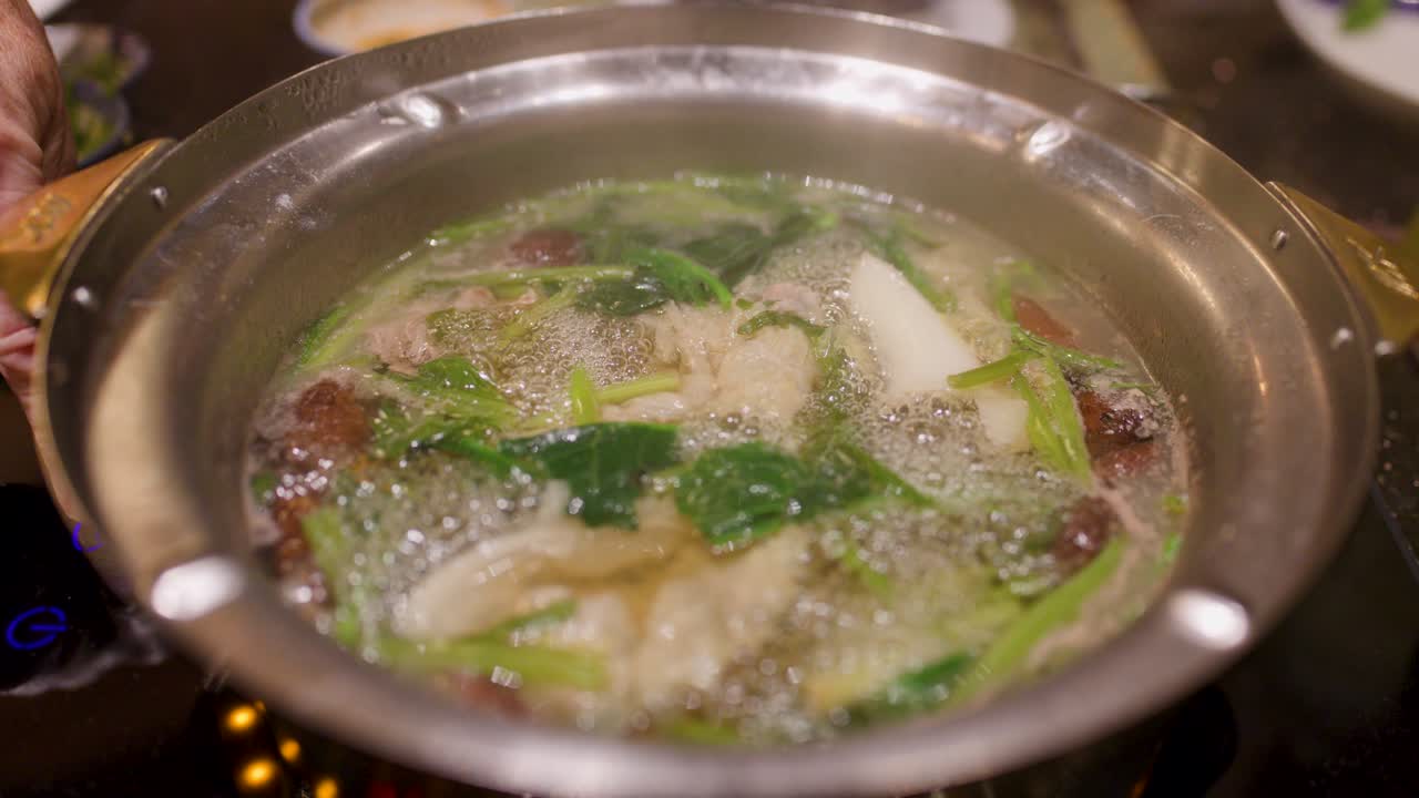 Overhead view of Asian hotpot broth boiling with assorted meats, leafy greens, mushrooms, and vegetables