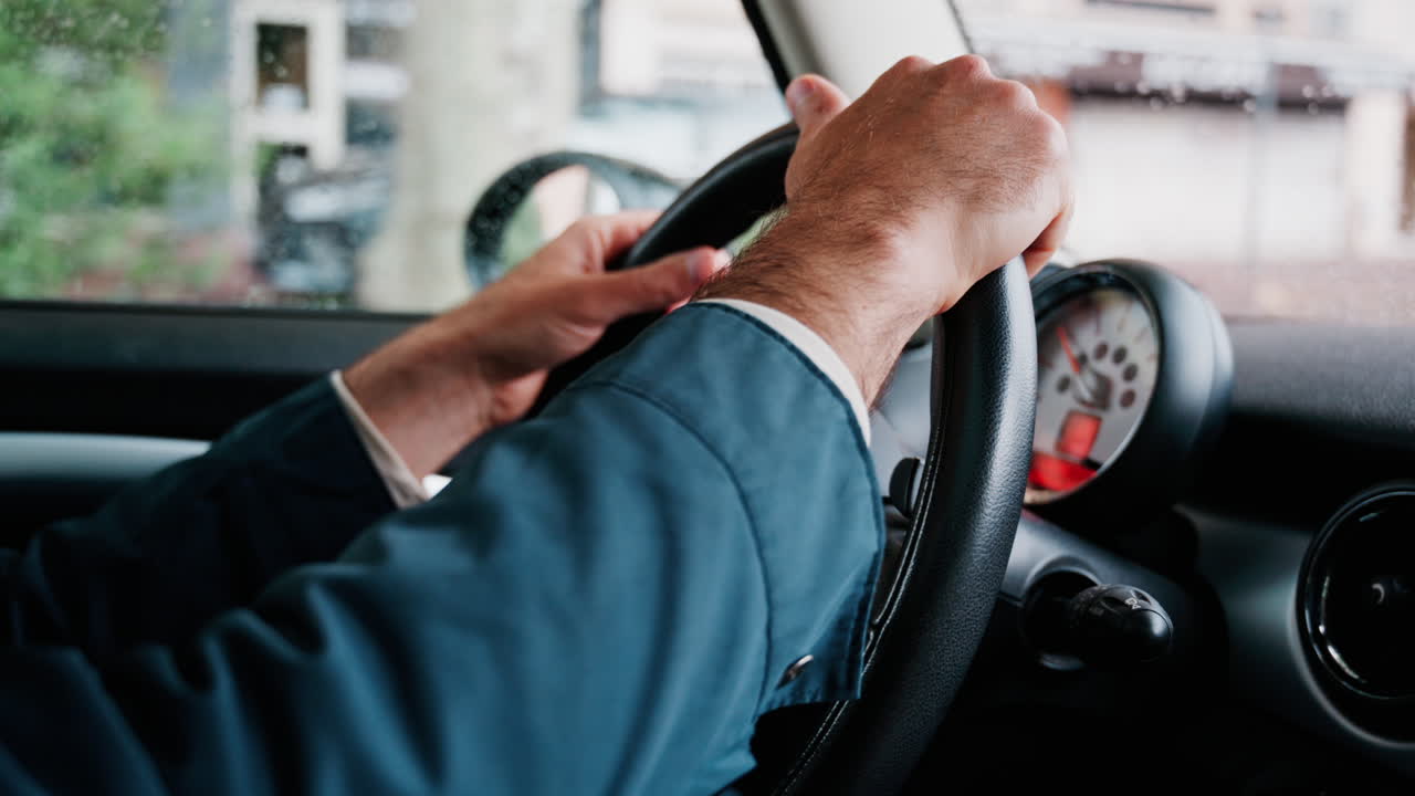 Close up of a man's hands on a steering wheel, driving a car on the road in the rain